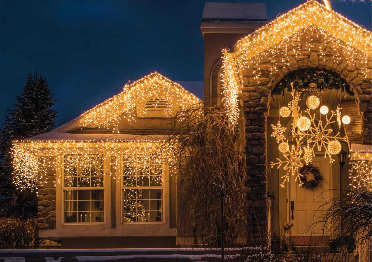 Warm white icicle lights and illuminated specialty decorations around a stone entryway
