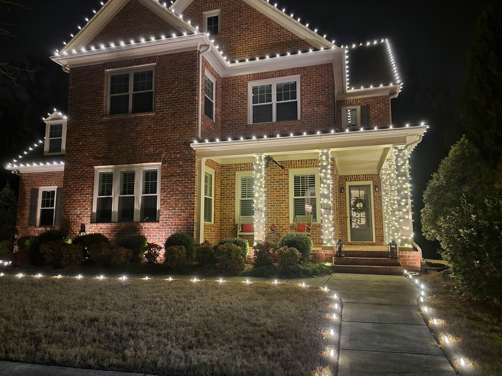 Warm white roofline lights and wrapped porch columns on a brick colonial