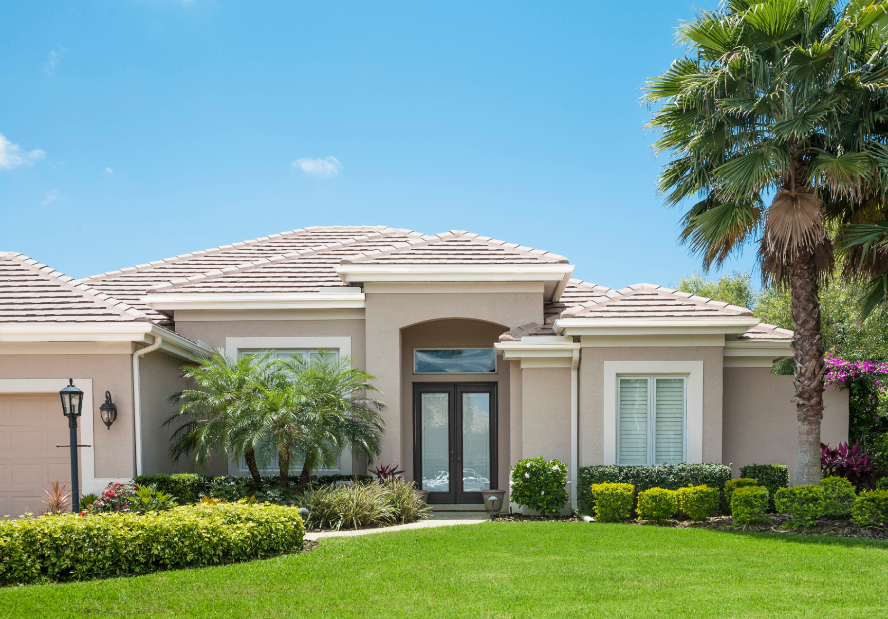 A pristine Florida home with manicured landscaping, tile roof, and palm trees under a clear blue sky